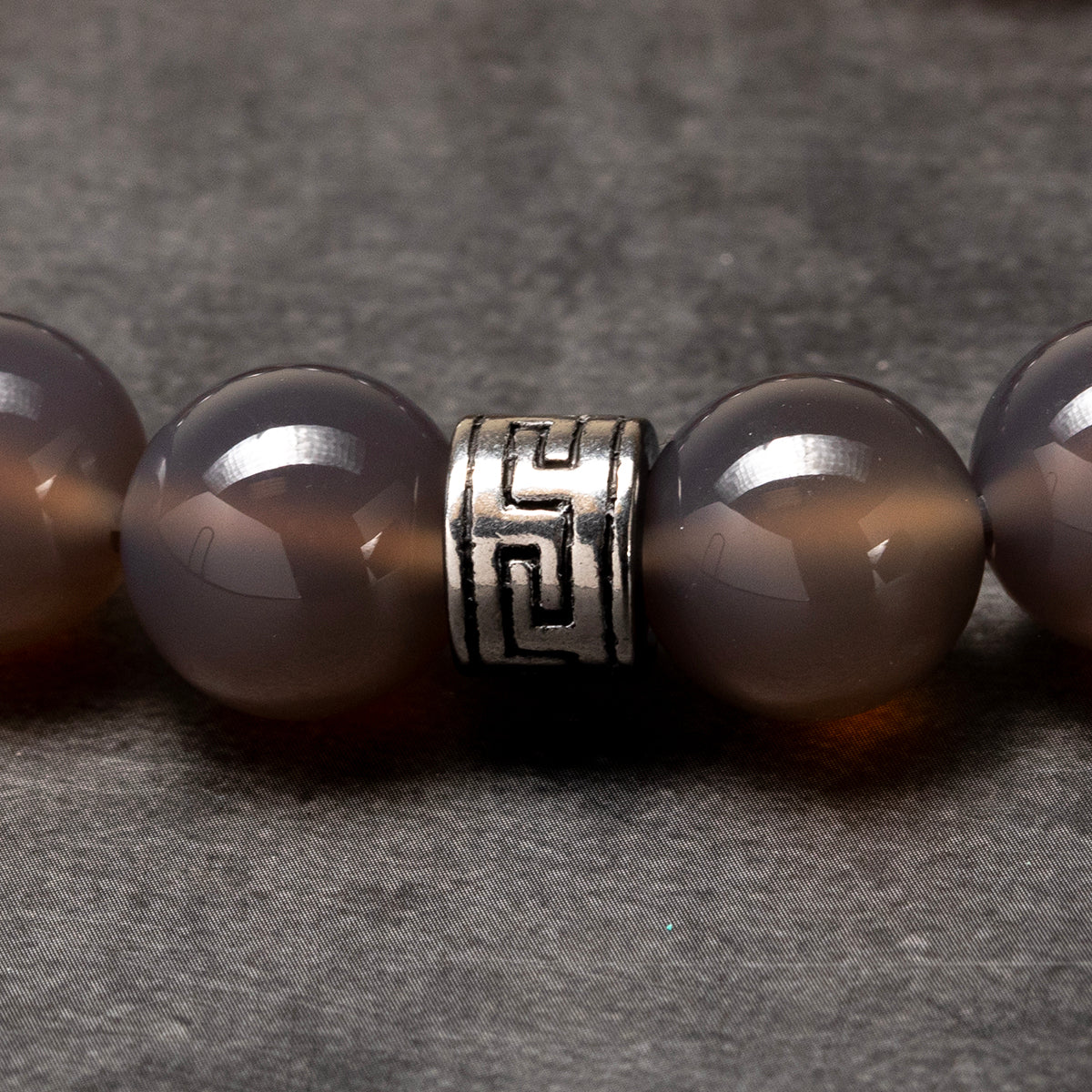 grey agate beaded bracelet with a stainless steel piece on a dark background