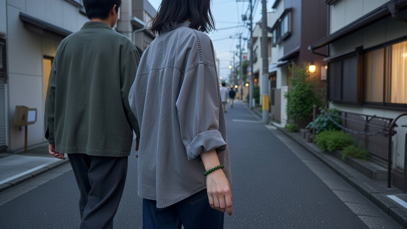 Young Japanese woman in white streetwear looks at her phone at a busy Japanese intersection, wearing a moss green quartz bracelet.