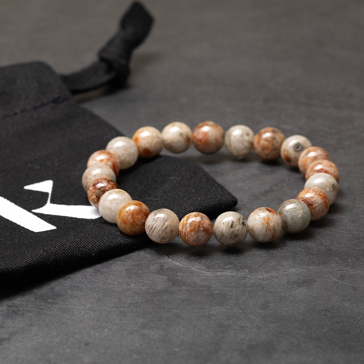 Beaded bracelet on a dark surface with a black drawstring bag in the background