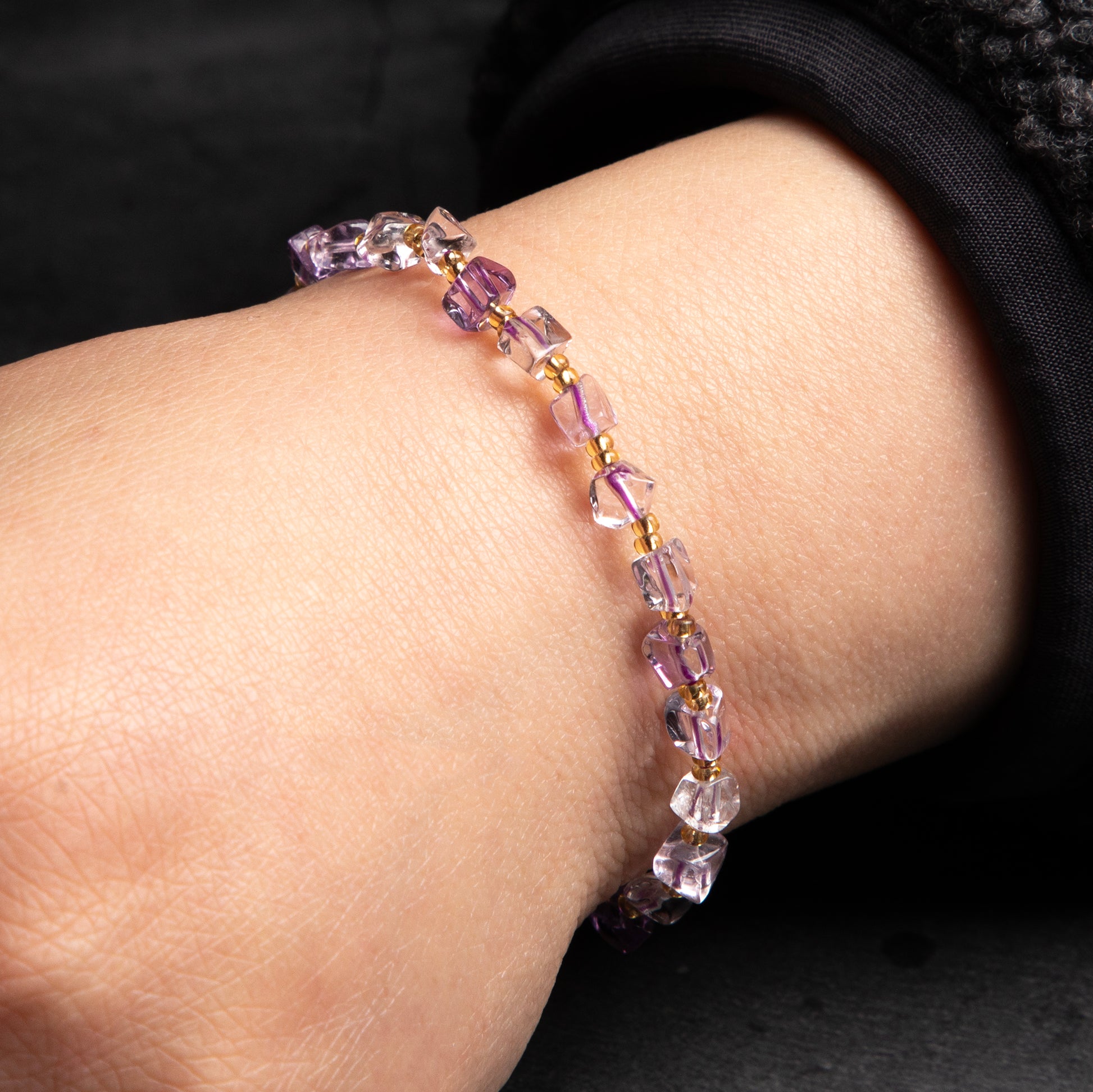Purple beaded bracelet on a wrist against a dark background