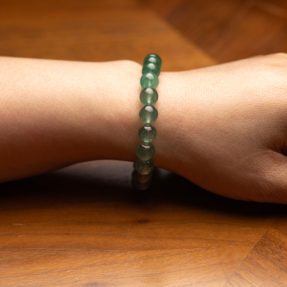 Green beaded bracelet on a wrist against a wooden background