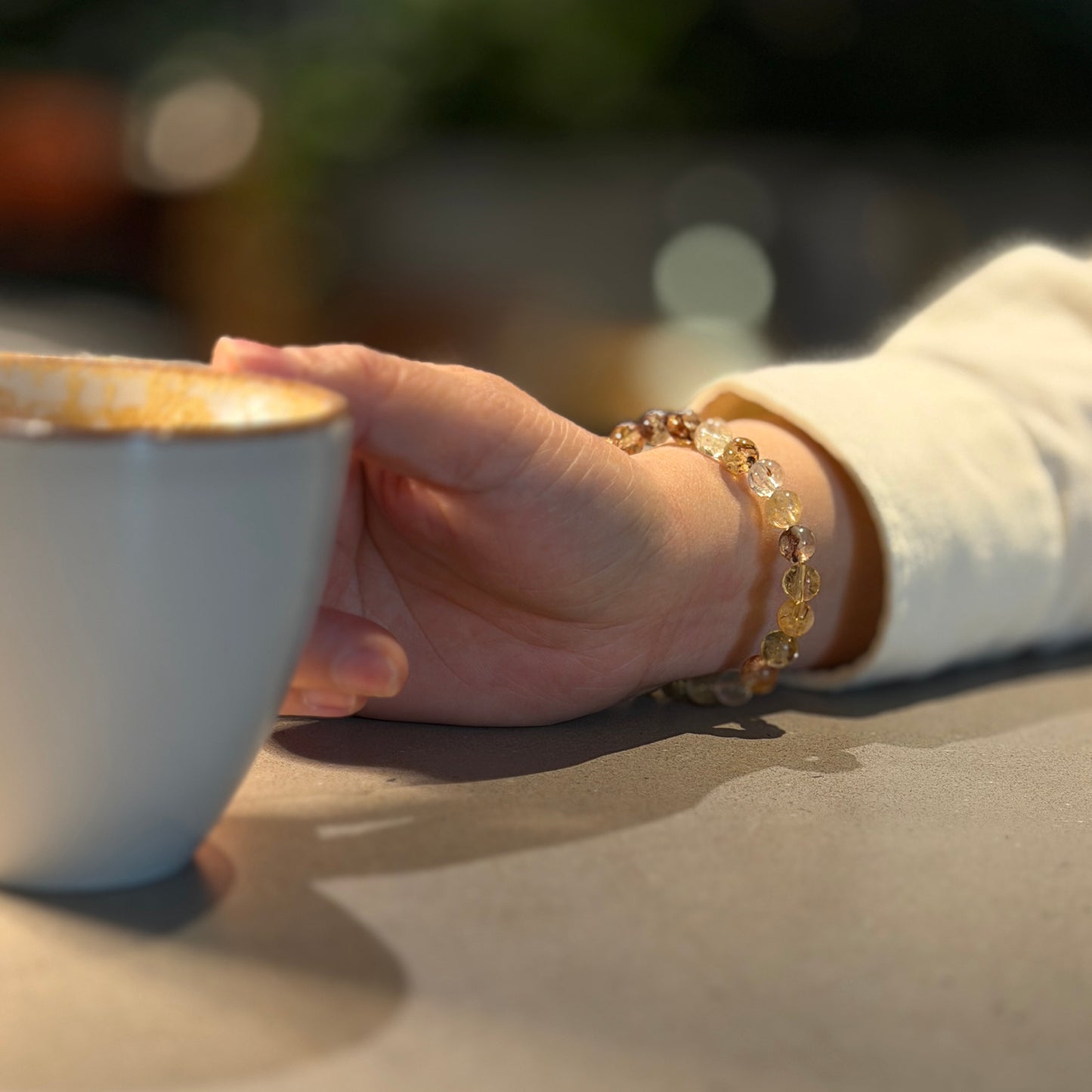 rutilated quarts with copper-gold rutile inclusions bracelet worn on the wrist of a woman holding a cup of coffee