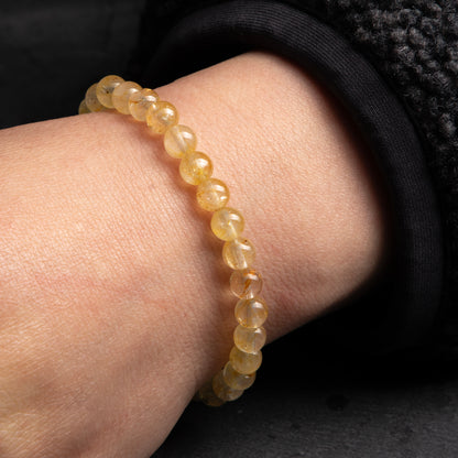 Close-up of a wrist wearing a beige beaded bracelet on a dark background
