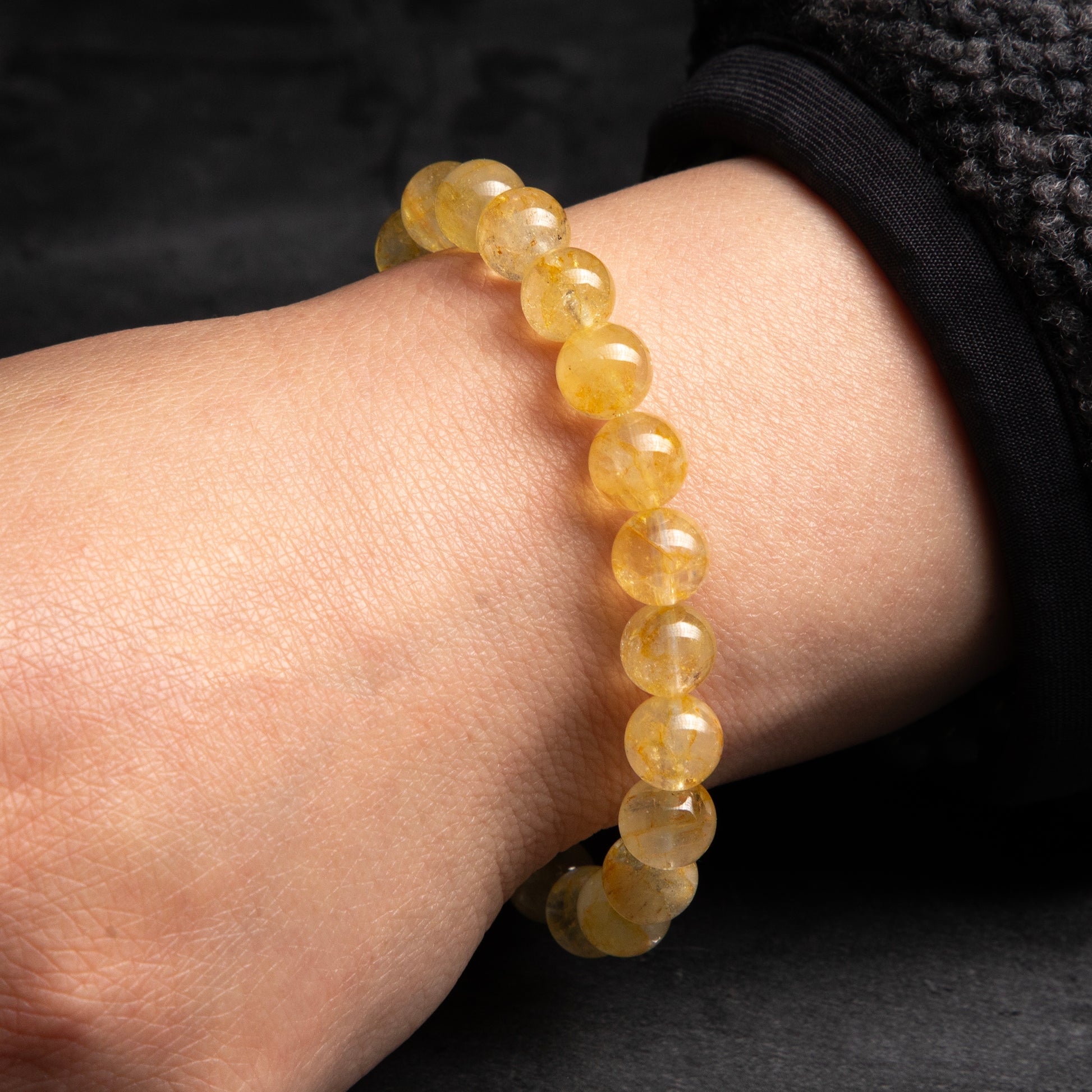 Yellow beaded bracelet on a wrist against a dark background