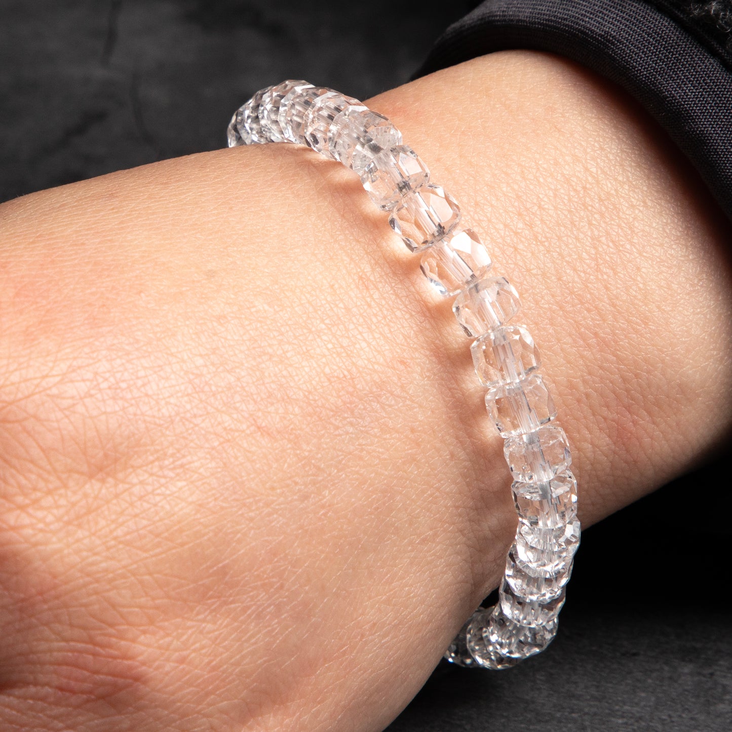 Close-up of a wrist wearing a clear beaded bracelet against a dark background