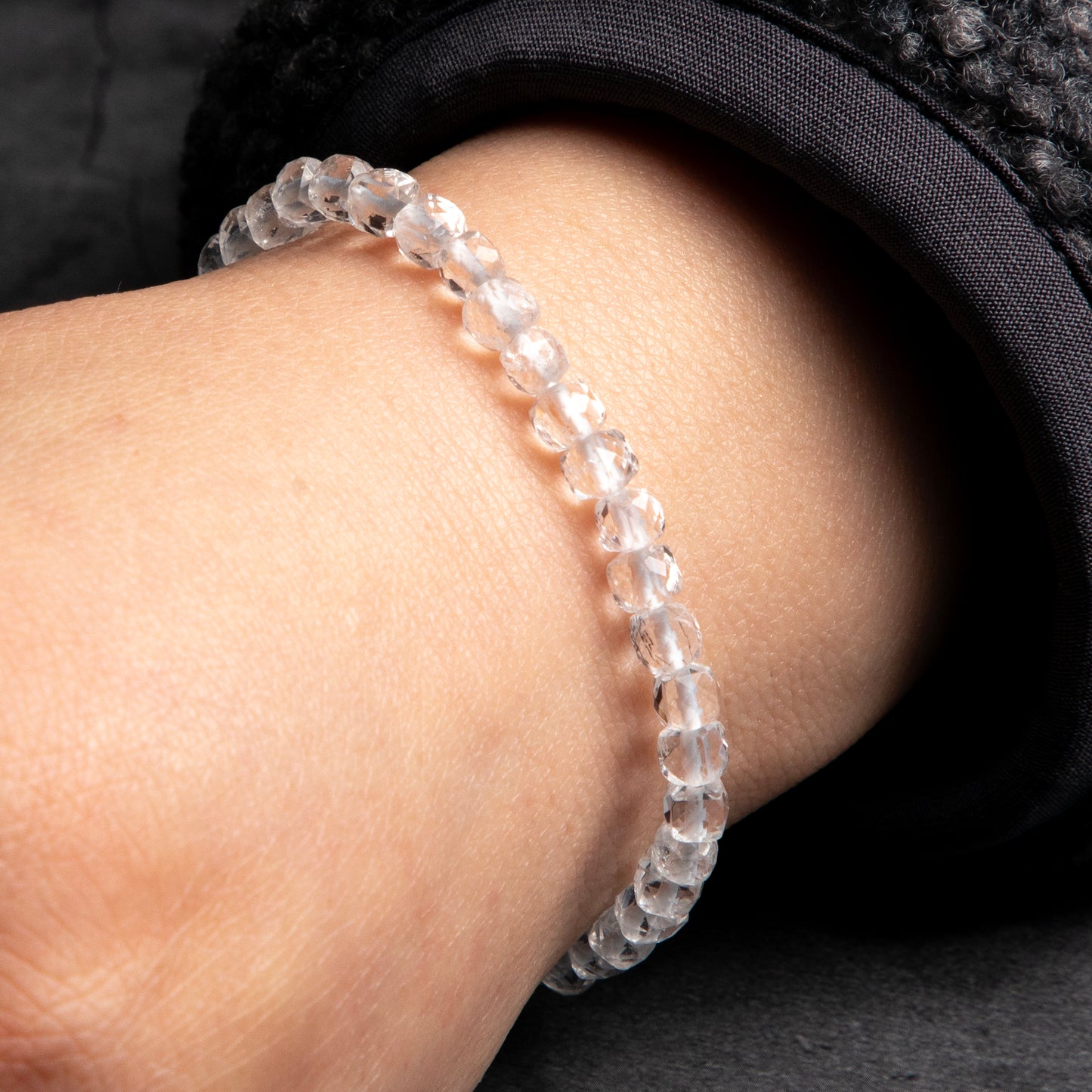 Close-up of a wrist wearing a clear beaded bracelet against a dark background