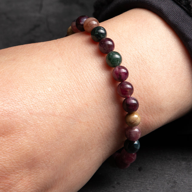 Multicolored beaded bracelet on a wrist against a dark background