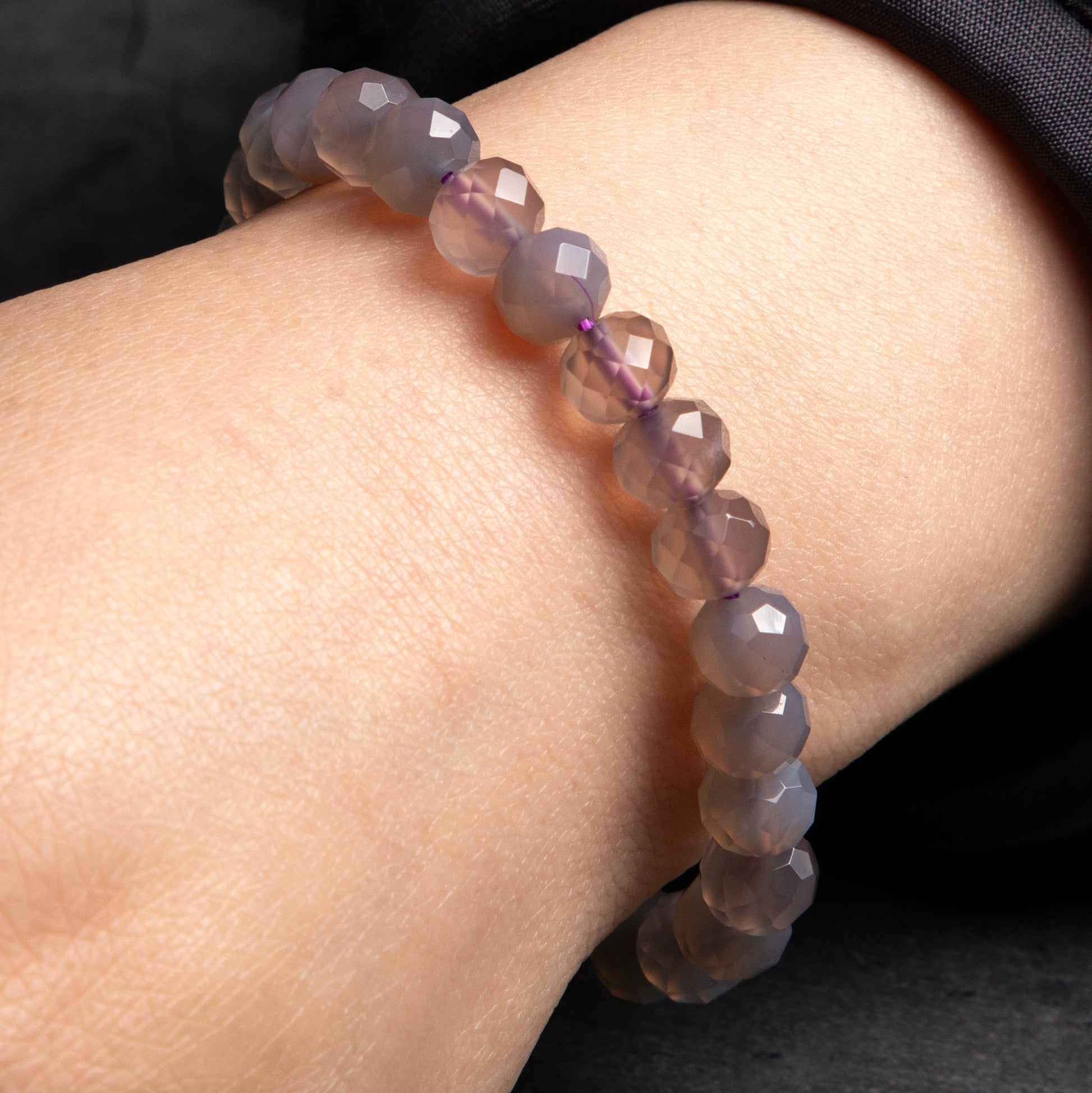 Purple beaded bracelet on a wrist against a dark background
