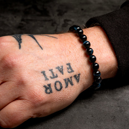 Hand with tattoos and a black beaded bracelet on a dark background