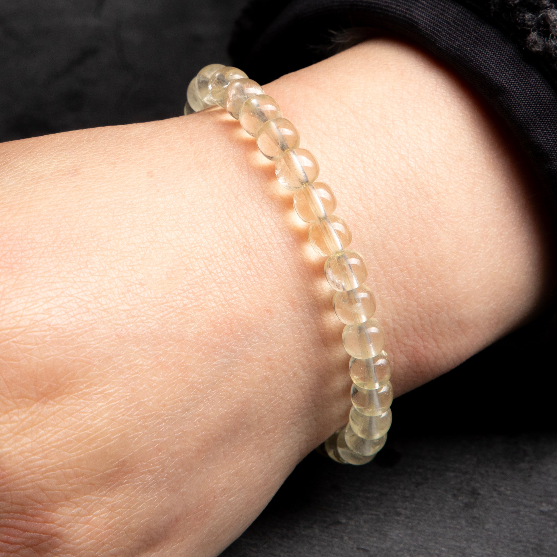 Close-up of a wrist wearing a bracelet with small, round, light-colored beads on a dark background.