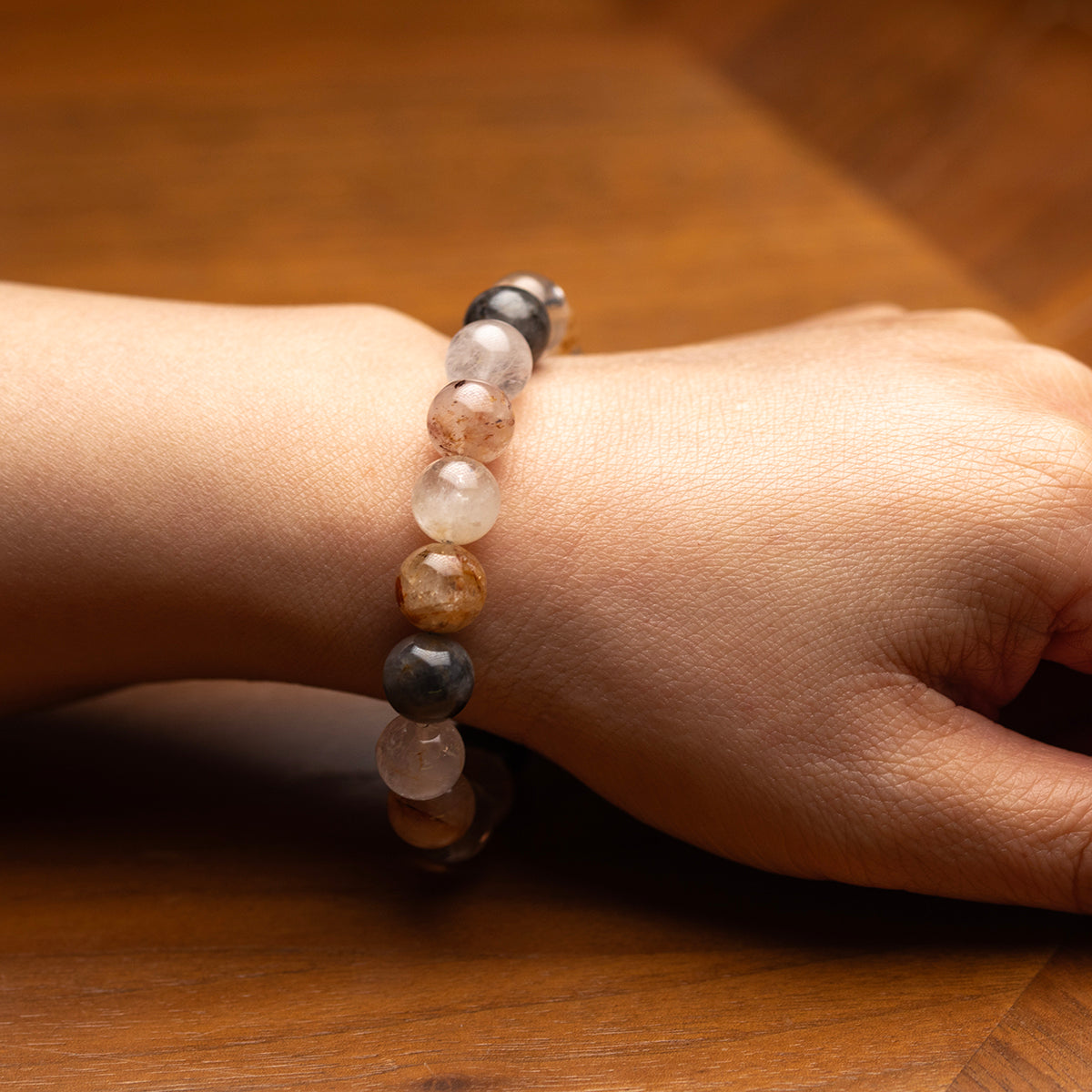 Close-up of a hand wearing a beaded bracelet on a wooden surface