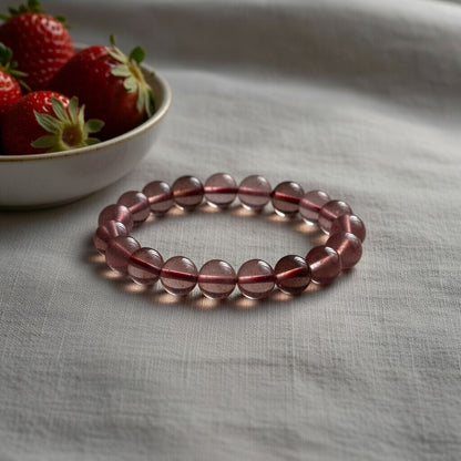 a pink bracelets rests on a grey bedcover next to a bowl of strawberries