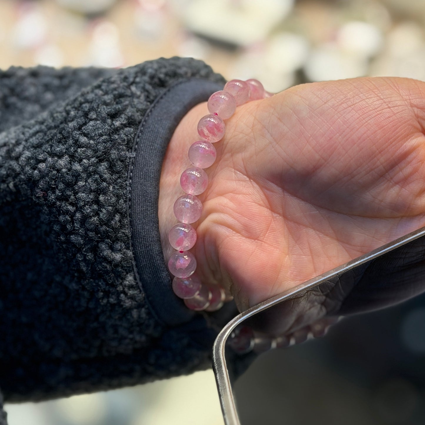 Hand wearing a pink beaded bracelet with a blurred background