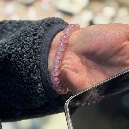 Hand wearing a pink beaded bracelet with a blurred background