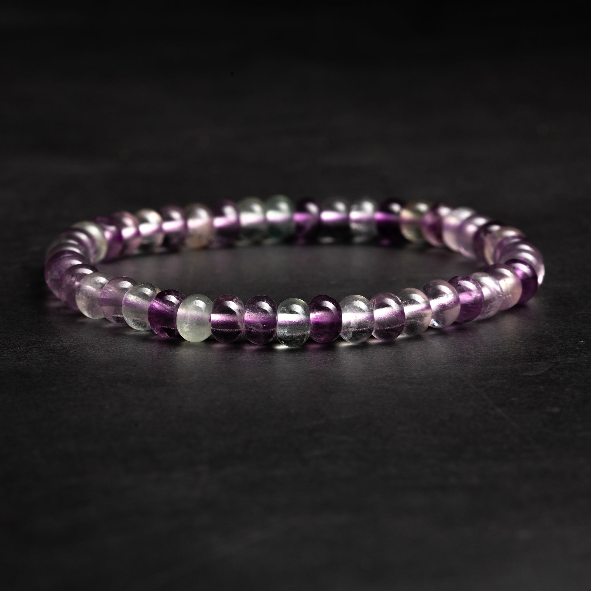 Beaded fluorite bracelet with purple, white, and clear beads on a dark background
