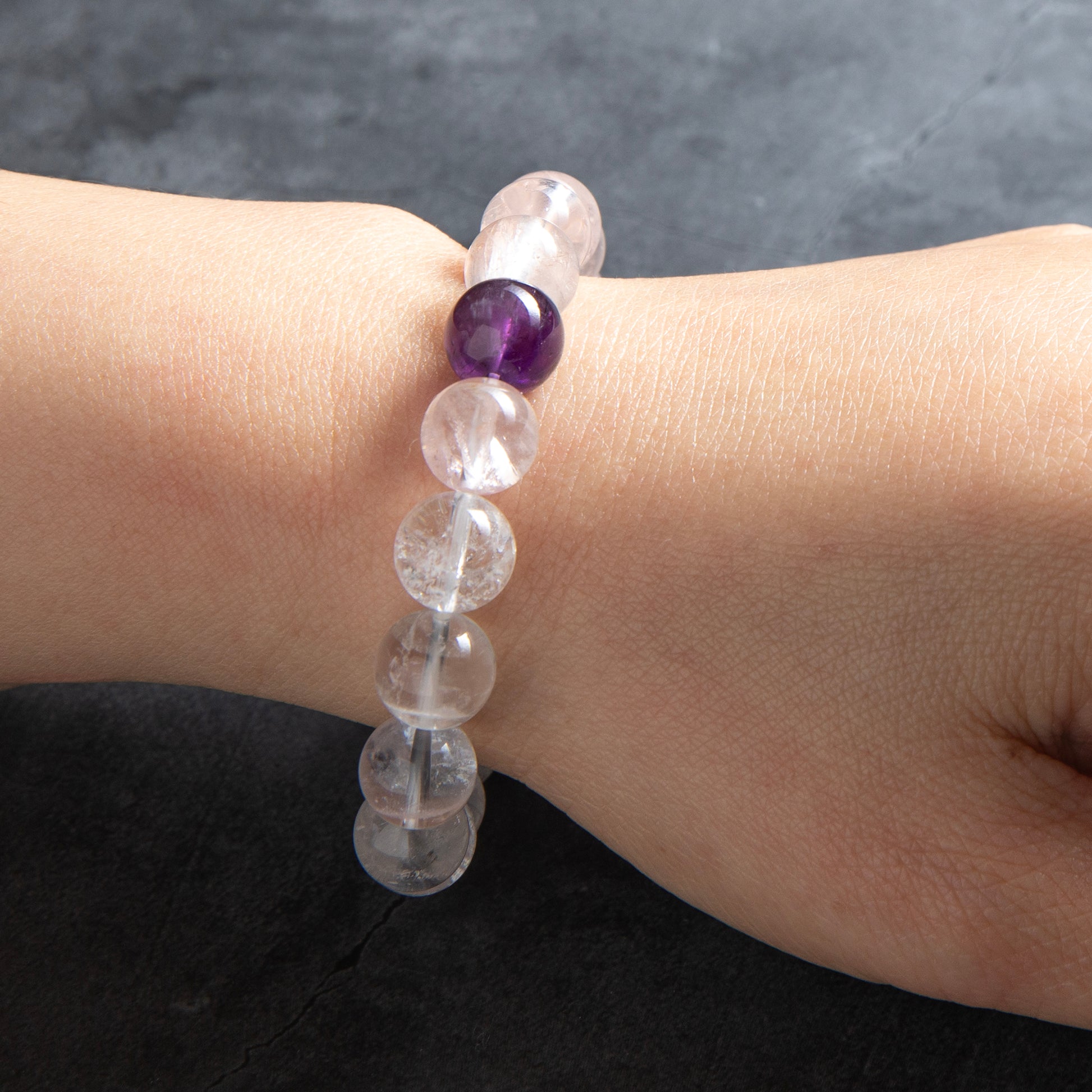Bracelet with clear and purple beads on a wrist against a dark background