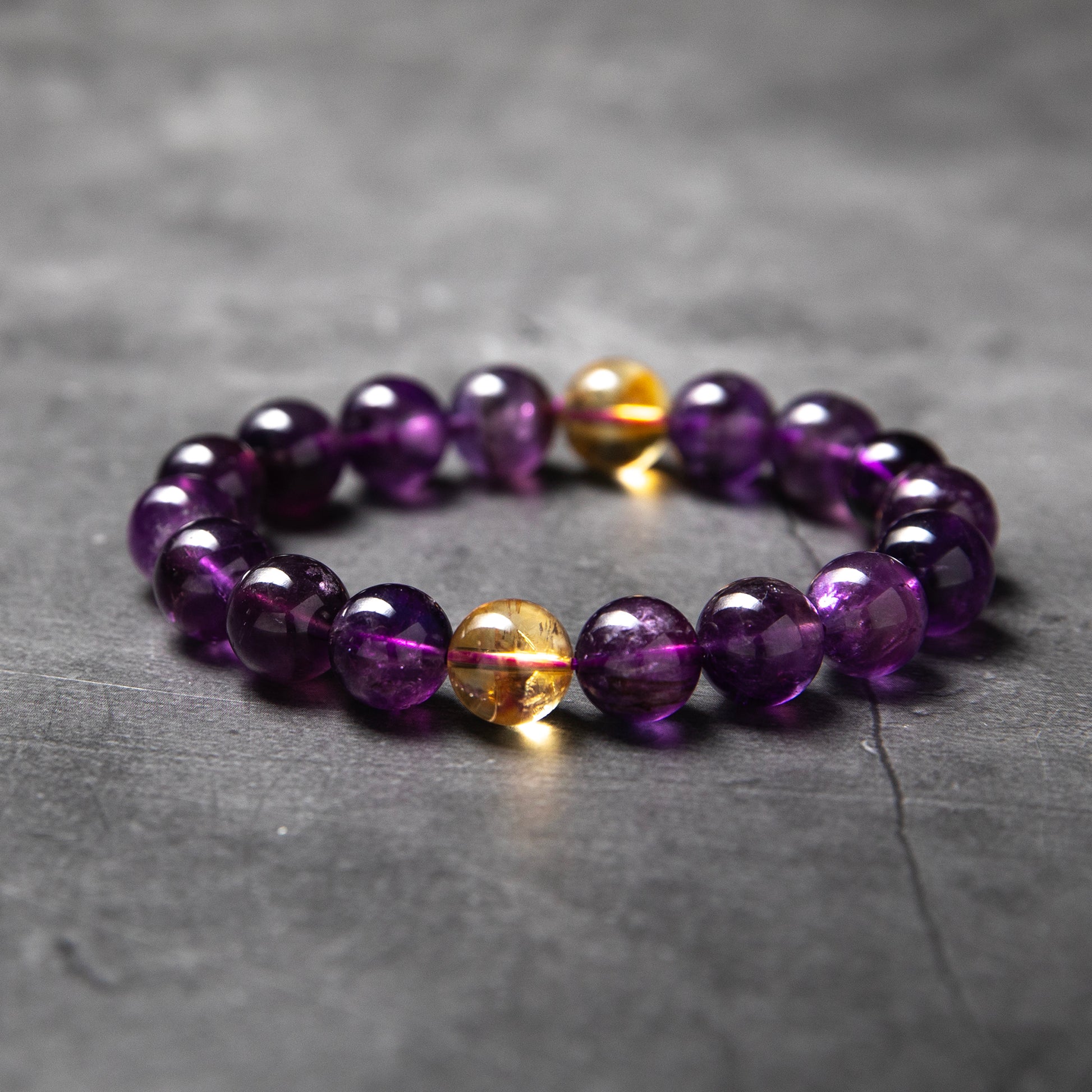 Beaded bracelet with purple and gold beads on a gray surface