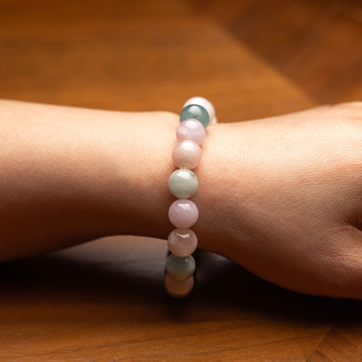 Close-up of a wrist wearing a bracelet with pink and green beads on a wooden surface