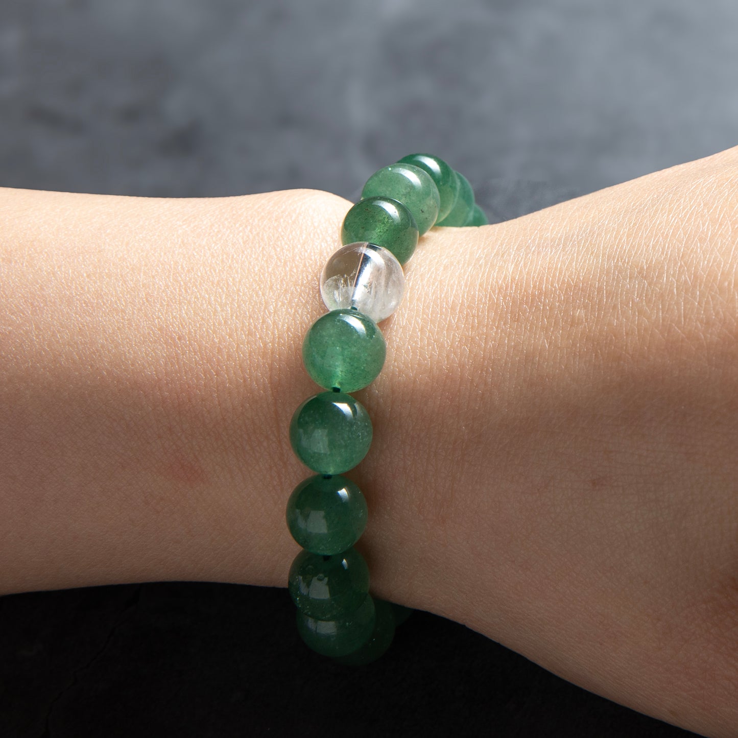 Green beaded bracelet on a wrist with a dark background
