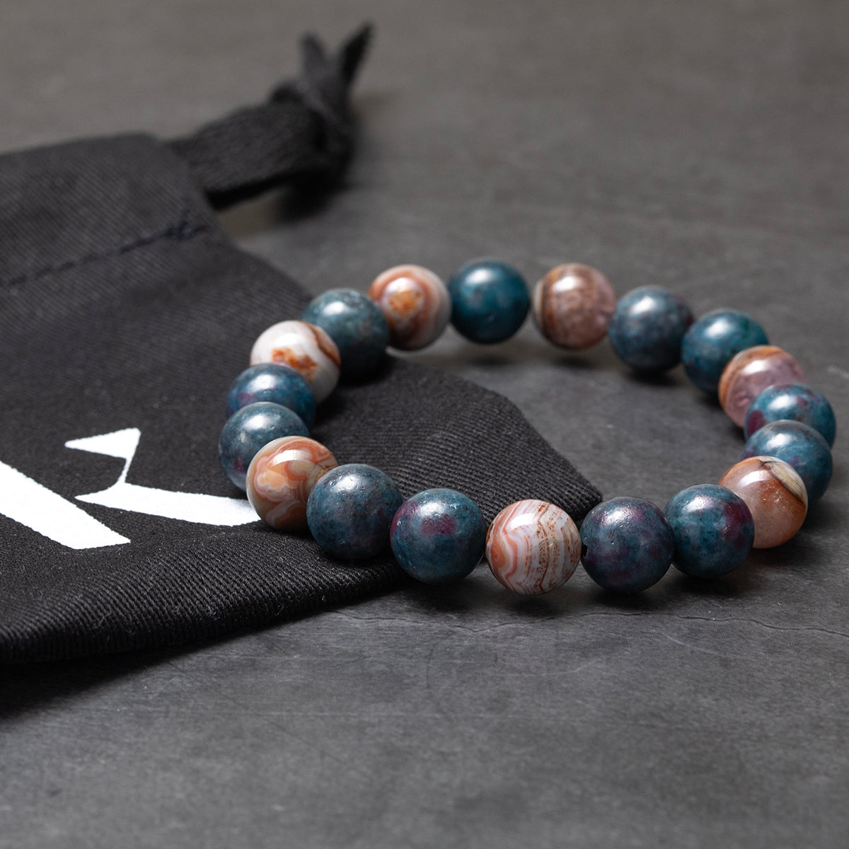 Multicolored beaded bracelet on a dark surface with a black bag featuring a logo.