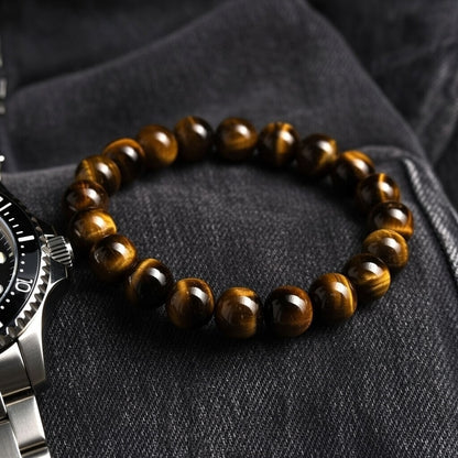a tiger eye bracelet sits on grey denim, a watch is just visible in the frame
