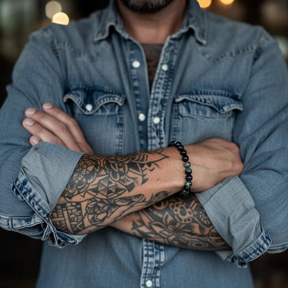Person wearing a denim jacket with tattooed arm and bracelet, blurred lights in the background